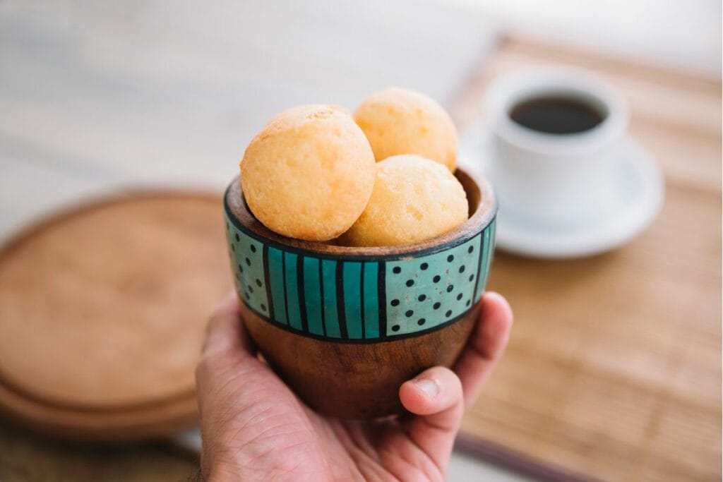 mini pães de queijo em uma cambuquinha com café ao fundo.